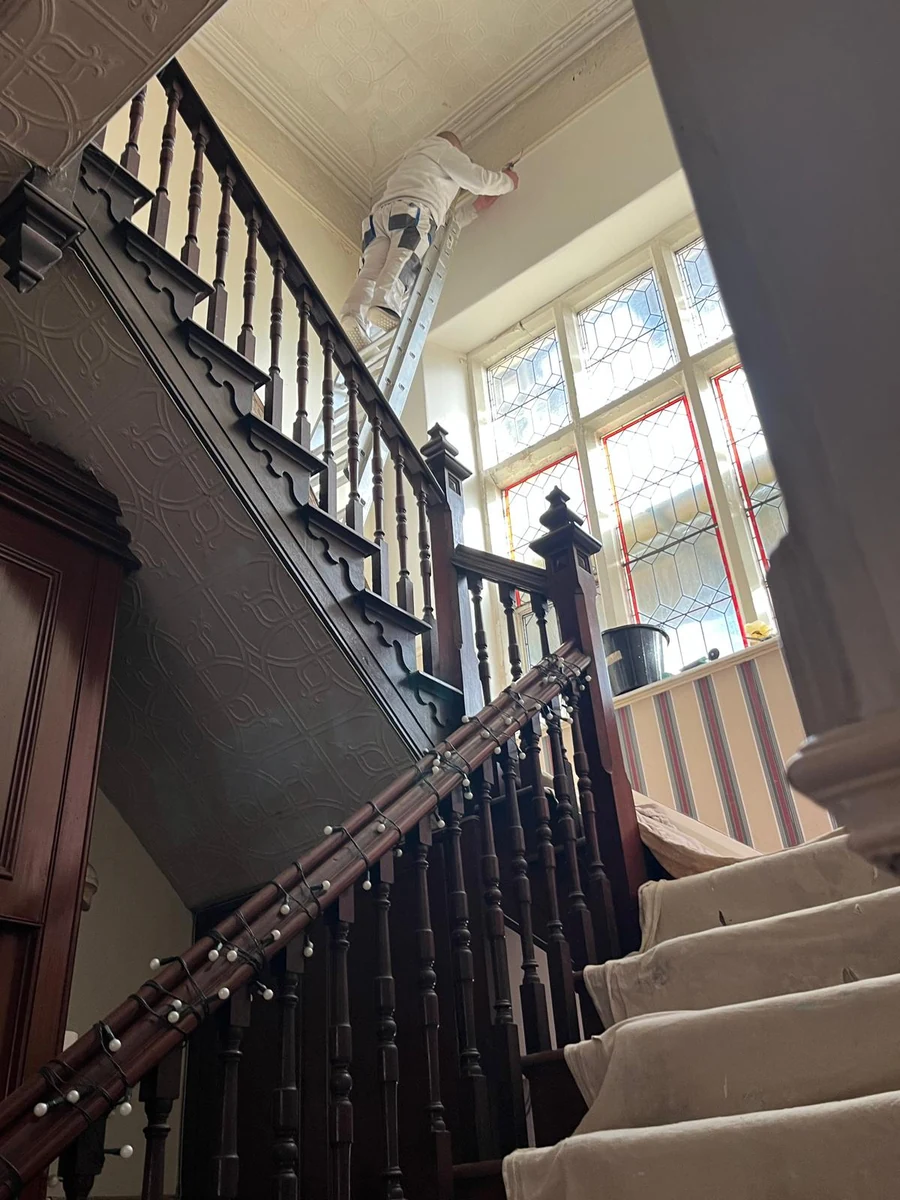 Decorator painting a double-height stairwell, Swansea